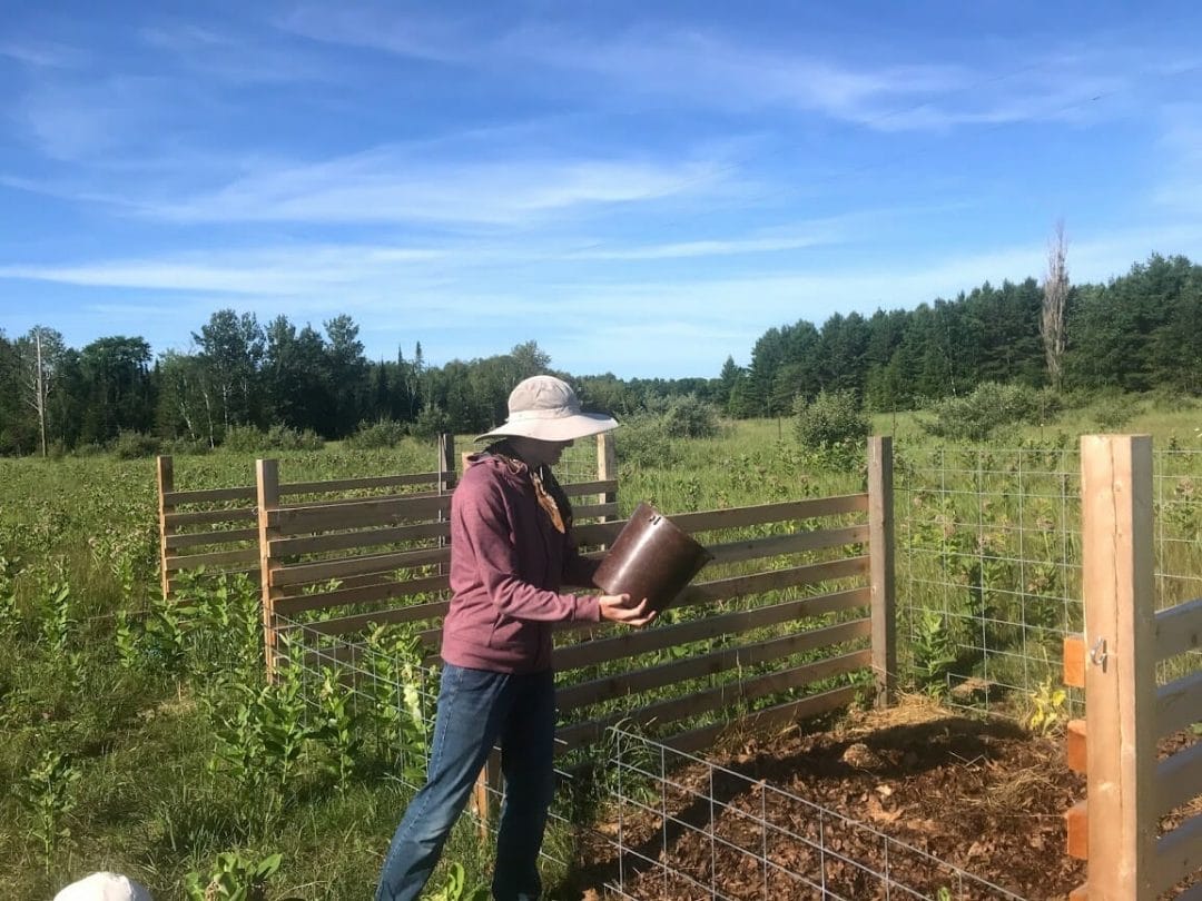 A woman dumps a bucket full of compost into the community compost pile