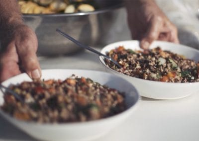 hands serving two bowls of locally grown vegetables and grains