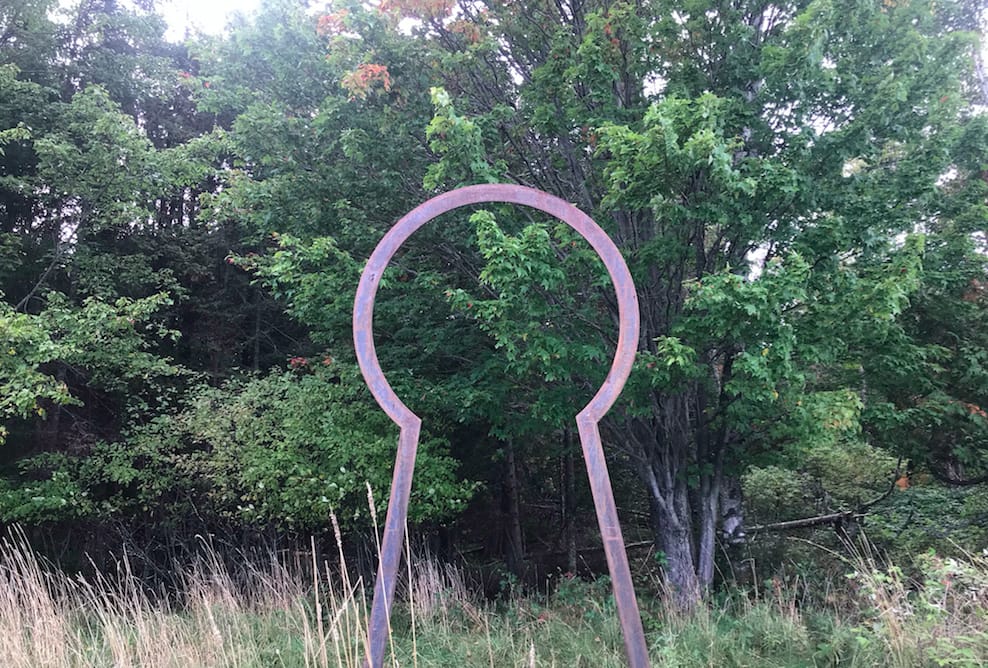 metal sculpture shaped like a key welcomes visitors to a forest path